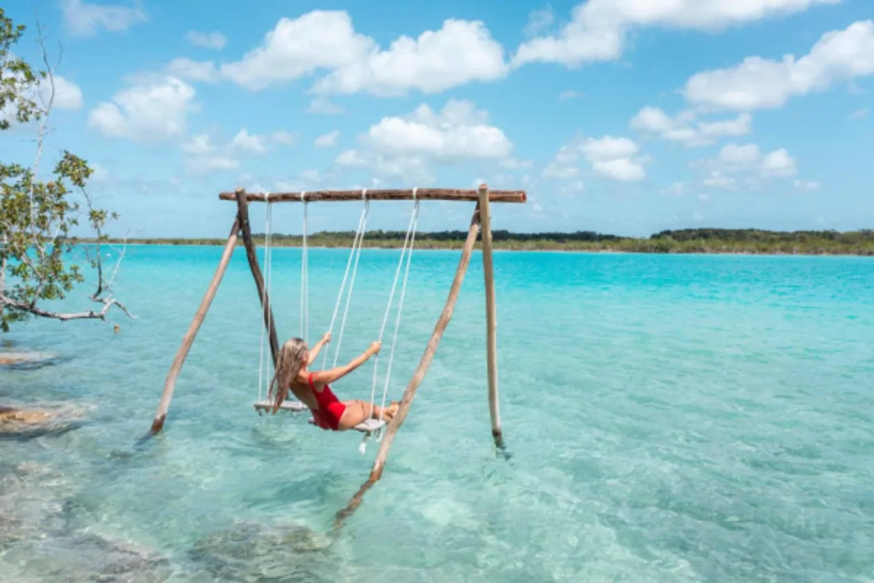 View of woman swinging on white sand beach relaxing and sunbathing by the lagoon in Mexico